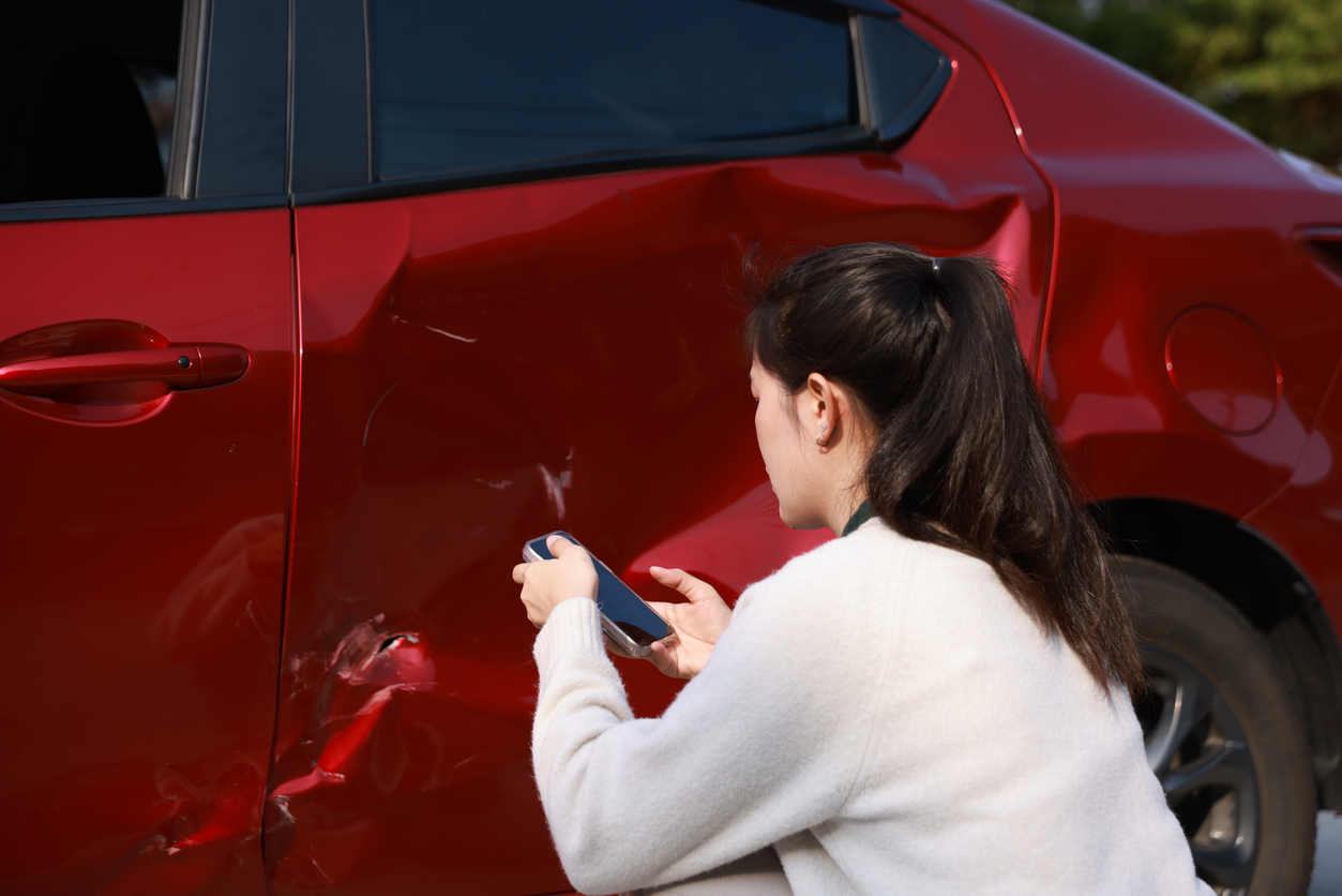 woman taking pictures of her vehicle after a car accident.